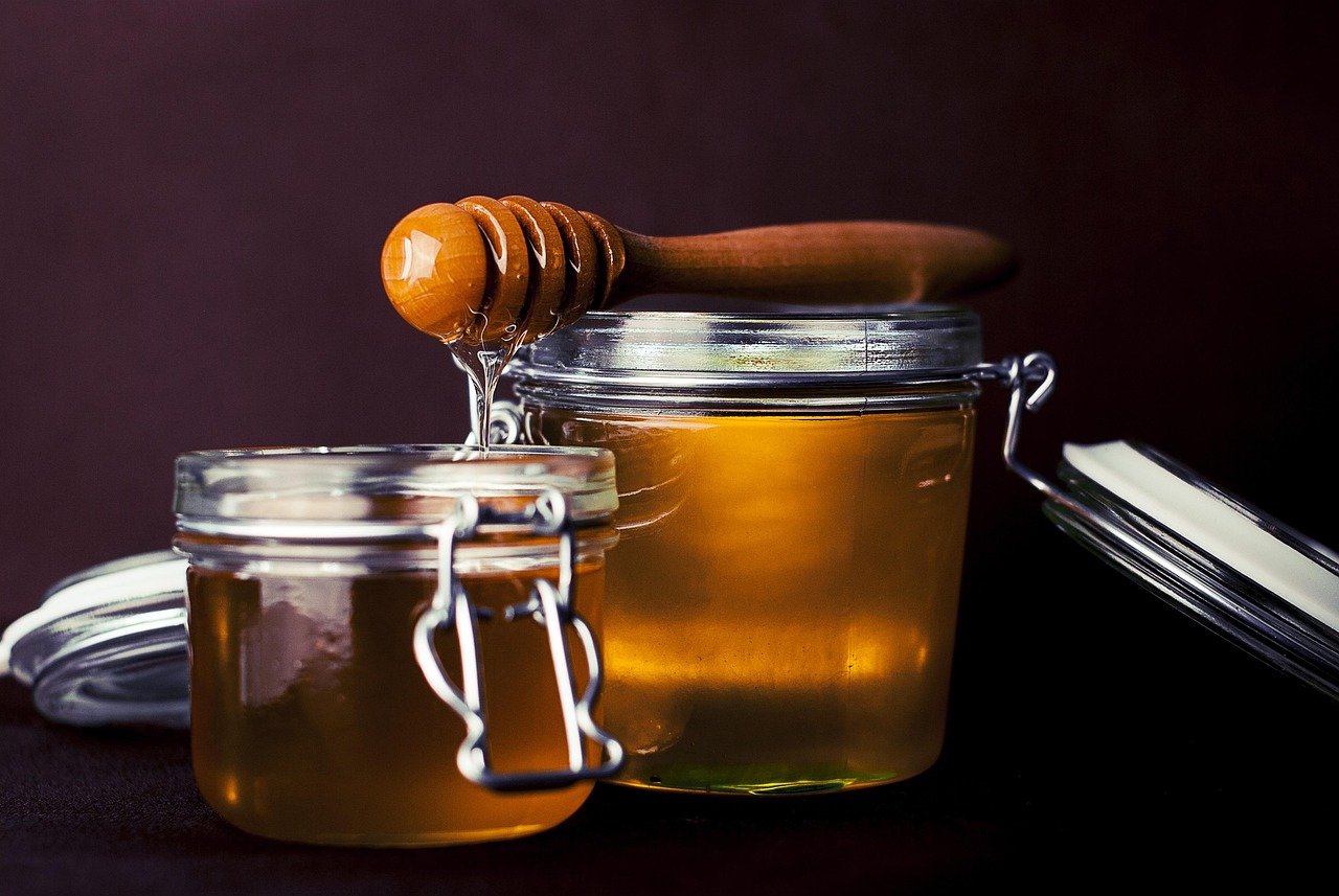 Golden honey from Mallorca in a glass jar surrounded by wildflowers and herbs.